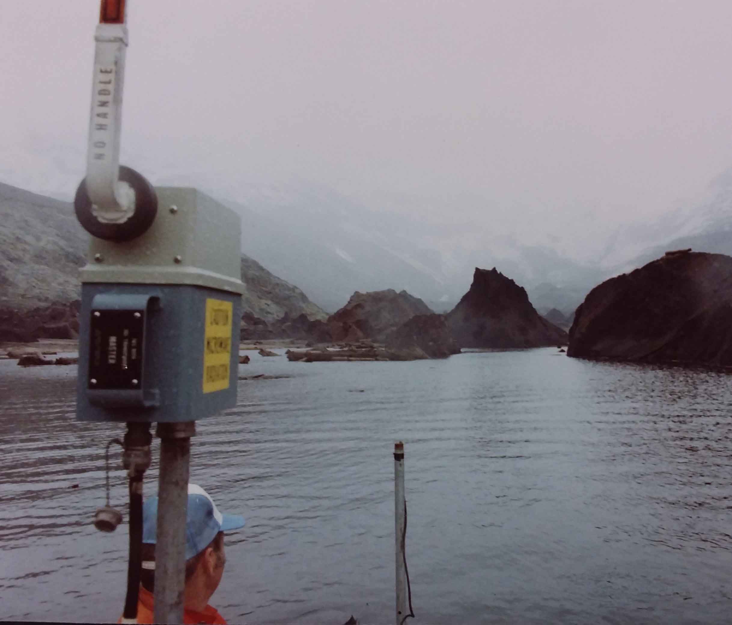May 5, 1981 - Leonard Nelson in aluminum boat in Bear Cove, West Arm of Spirit Lake with debris avalanche hummocks. Microwave trisponder range finder in boat for use in bathymetric mapping.  USGS K. Tanner